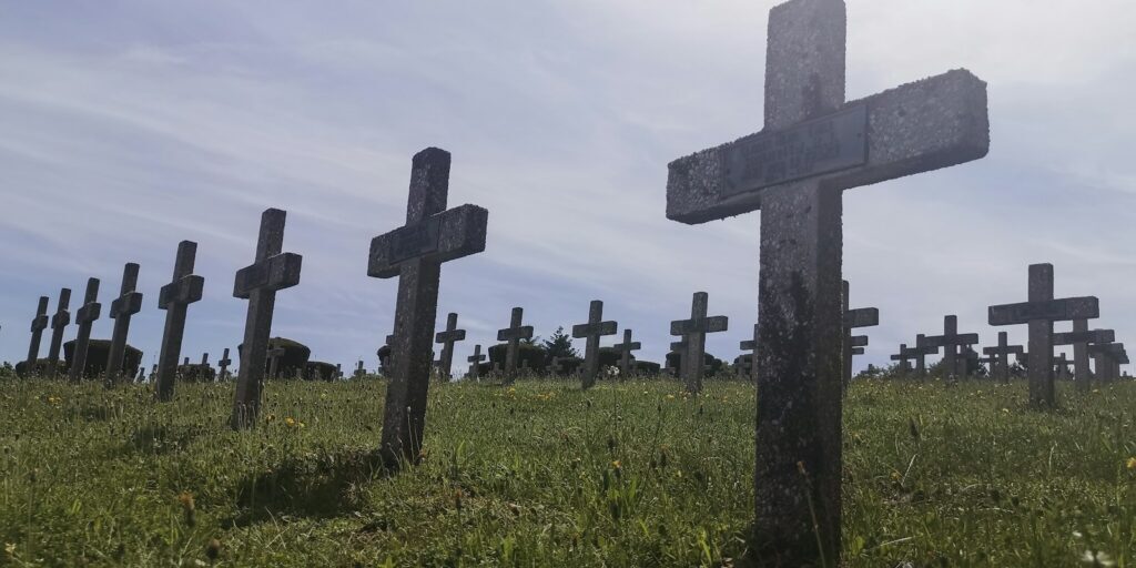 gray cross on green grass field under white clouds during daytime