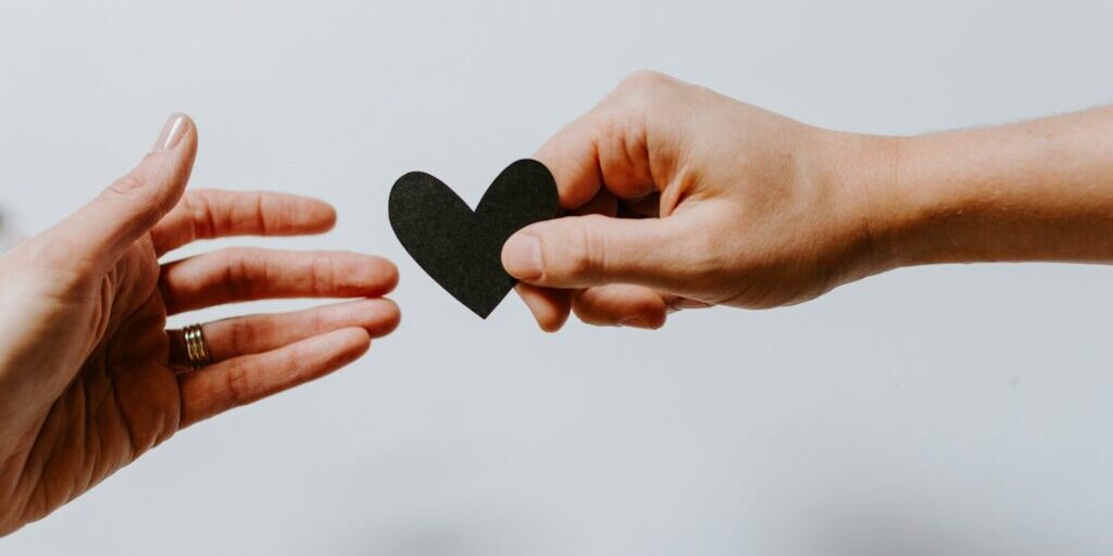 person reaching black heart cutout paper